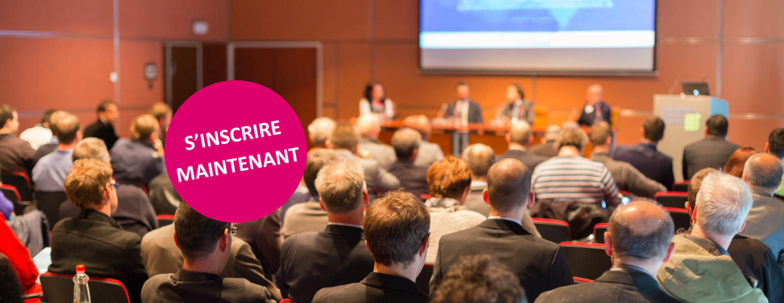 Salle de conférence pleine avec quatre personnes sur la scène qui discutent ensemble